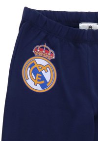 Marineblauwe trainingsbroek met elastische tailleband en een wit-gouden Real Madrid voetbalclublogo aan de linkerkant.
