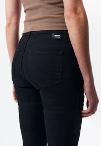 Jeans de mezclilla elásticos negros con un diseño ajustado, que cuentan con bolsillos traseros y una etiqueta de la marca. Textura suave, cintura de altura media. Sin herrajes visibles.