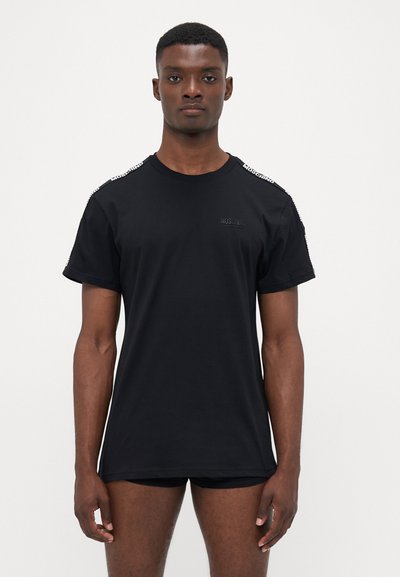 T-shirt en coton noir à manches courtes, avec un logo sur la poitrine et des accents à motifs sur les épaules. Design simple à coupe régulière.