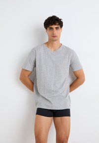 T-shirt en coton gris à manches courtes et col en V, porté avec un short noir ajusté. Silhouette simple et moderne.