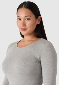 Šedý dlouhý rukáv top vyrobený z měkké, elastické látky s kulatým výstřihem a hladkým povrchem, s detaily švů podél stran.