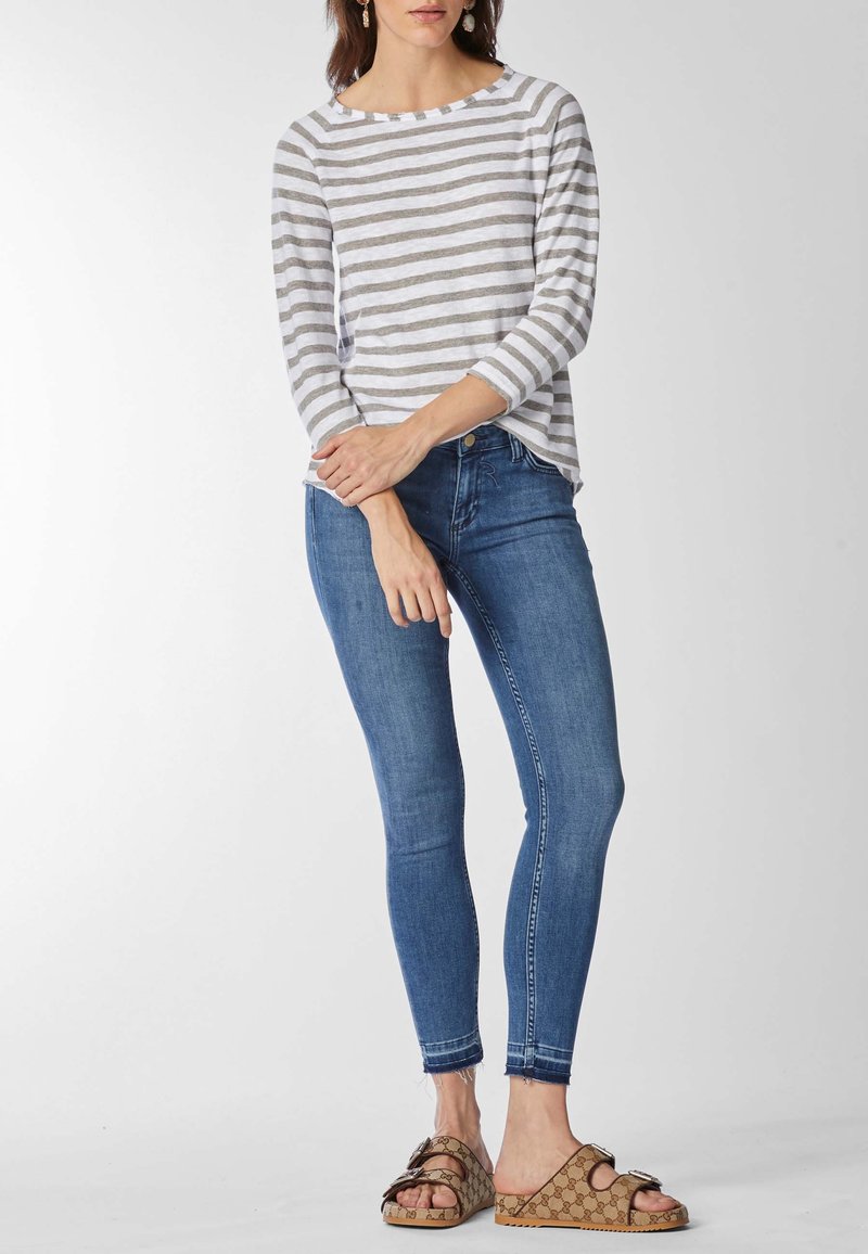 Maglietta a maniche lunghe grigio e bianco a righe leggera abbinata a jeans blu aderenti e sandali marroni testurizzati con accenti a motivo.