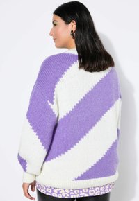 Übergroßer Strickpullover mit diagonalen Streifen in Lavendel und Weiß. Weiche Textur mit gerippten Bündchen und Saum. Über einem gemusterten Oberteil getragen.