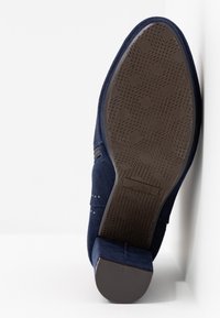 Chaussure en daim bleu marine avec une semelle en caoutchouc texturée, dotée d'un petit talon carré et d'un motif discret en losanges sur la semelle extérieure.