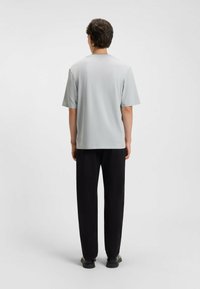 Lys grå t-shirt med korteærmer, afslappet pasform, rund halsudskæring og glat tekstur, parret med løse sorte bukser og sorte sko.