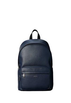 Navy blue leather backpack with a front zippered pocket and black top handle, featuring a small silver Calvin Klein logo on the pocket.