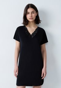 Abito corto nero a maniche corte con scollatura a V e dettagli in pizzo, vestibilità morbida e texture liscia. L'orlo è leggermente curvo ai lati.