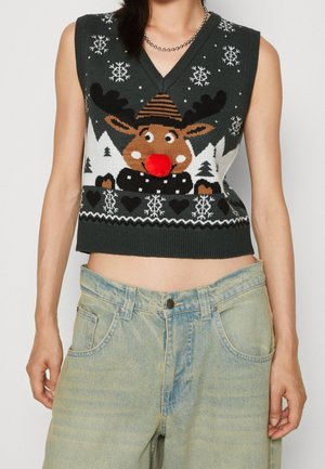 Veston en pull avec un renne de dessin animé avec un nez pompon rouge, des flocons de neige et des arbres, porté avec un jean bleu clair et un collier de perles.