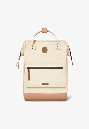 Sac à dos en toile beige avec un fond et une poignée en cuir marron, équipé d'une poche avant zippée et d'un badge logo circulaire en haut.