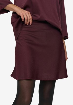 Burgundijas krāsa svārki, kas izgatavoti no gludas auduma, ar izplestu dizainu un līdz ceļiem garumu. Apvienoti ar melnajiem zeķubiksēm, rādot vienkāršu, elegantu stilu.