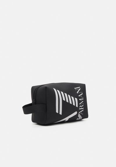 Trousse cosmétique noire zippée avec des motifs géométriques blancs et un logo. Matériau doux et texturé avec une poignée latérale pour un transport facile.