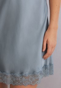 Jedwabna niebieska sukienka z ozdobnym koronkowym wykończeniem. Gładki materiał ma delikatny połysk, a falbana koronkowa w pasującym odcieniu.