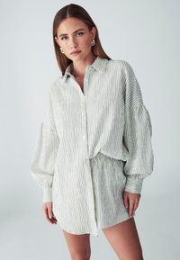 Pruhované šaty košeľového štýlu s dlhým rukávom v svetlozelených a bielych farbách. Majú zapínanie na gombíky vpredu, voľný strih a zošitý pás pre nastaviteľný štýl.