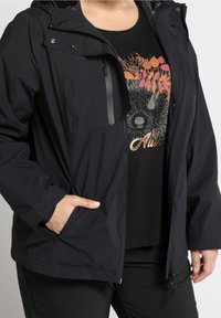 Zwarte waterdichte jas met een capuchon, ritssluiting en drukknoopsluitingen, twee zijzakken en een borstzak met rits; gladde textuur.