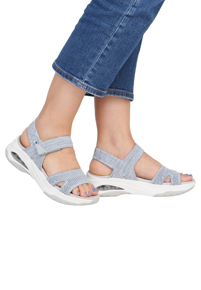 Sandales gris clair avec des sangles en maille élastique et une semelle blanche rembourrée, comportant une bulle d'air au talon pour un soutien supplémentaire.