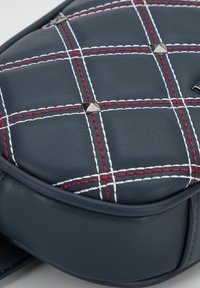 Borsa in finta pelle blu navy con un motivo trapuntato, decorata con cuciture bianche e rosse e borchie a forma di piramide metalliche.