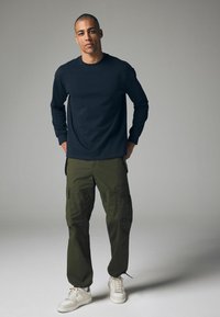 Marineblaues Langarmhemd, olivgrüne Cargo-Hosen mit Seitentaschen und weiße Sneaker. Lässige Passform und glatte Stoffoberflächen.