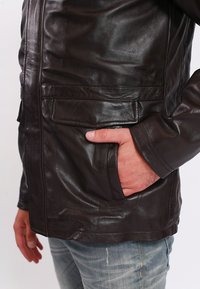 Dunkelbraune Lederjacke mit glatter Textur, ausgestattet mit zwei Vordertaschen und einem Reißverschluss. Der Kragen ist schlicht und ohne Verzierungen.