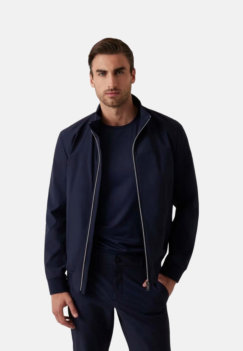 Giacca zip-up blu navy con alto colletto e sottili accenti bianchi. Realizzata in tessuto liscio, presenta cuciture orizzontali e una vestibilità slim.