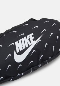 Musta pehmustettu kangastuote, jossa on valkoinen Nike-logo ja useita pieniä valkoisia Nike-swoosh -painatuksia pinnalla.