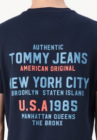 Tengerészeti pamut póló, merész, több színű felirattal világoskék, piros és fehér színben, amely a márkanevet és a New York-i helyszíneket tünteti fel.