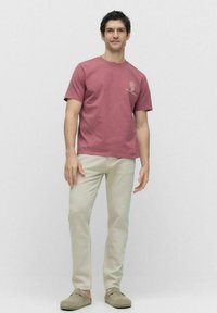 Mørkerød bomulds t-shirt med korte ærmer og et kaktusprint på brystet, parret med lysebeige bukser og grå slip-on sko.