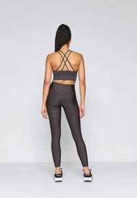 Tumehall sportmüts ristseljaga rihmadega, millele on sobitatud kõrge puusaga retuusid, mille alumistes osades on tekstuuriga muster, ning mustad spordijalatsid.