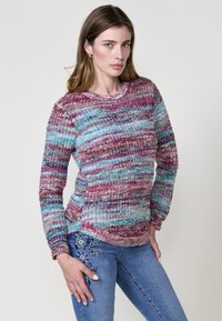 Suéter de punto multicolor con franjas de rosa, azul y crema. Cuello redondo y mangas largas, combinado con unos pantalones vaqueros bordados.