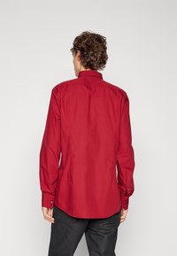 Rotes Langarmhemd mit spitzem Kragen, Knopfleiste und geschwungenem Saum. Glatter Baumwollstoff mit tailliertem Schnitt.