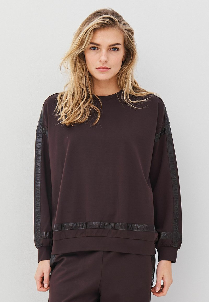 Musthave mustripsiga must nokk, millel on nahataolised aktsendid õlgadel ja servades. Pehme tekstuur ja lahtine lõige, ümar kaelus.