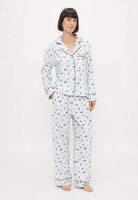 Lichtblauw pyjama-set met een knoopsluiting shirt en losse broeken met een bloemenpatroon in donkerrood en groen. Zwarte bies accentueert de randen.