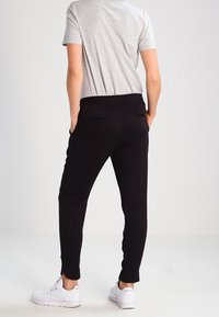 Černé joggingové kalhoty s elastickým pasem, bočními kapsami a zúženými nohavicemi, v kombinaci se šedým tričkem a bílými teniskami. Hladká textilie.