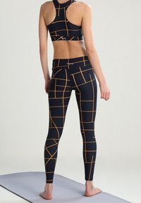 Top corto sportivo nero e leggings con motivo a griglia geometrica arancione. Il tessuto appare liscio ed elasticizzato, adatto per l'abbigliamento sportivo.
