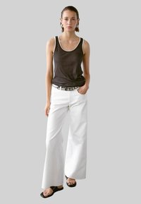 Zwarte tanktop met witte afwerkingen, gecombineerd met losse witte broeken. Model draagt een zilveren riem en zwarte sandalen. Eenvoudig, modern ontwerp.