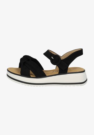 Schwarze Wildleder-Sandale mit einem gedrehten Vorderriemen, verstellbarem Knöchelriemen und einer weißen Plateausohle mit einer schwarzen Akzentlinie.