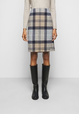 Spódnica w kratę sięgająca kolan w odcieniach beżu, szarości i granatu, noszona z beżową bluzką z długim rękawem oraz czarnymi kozakami do kolan na jasnym tle.