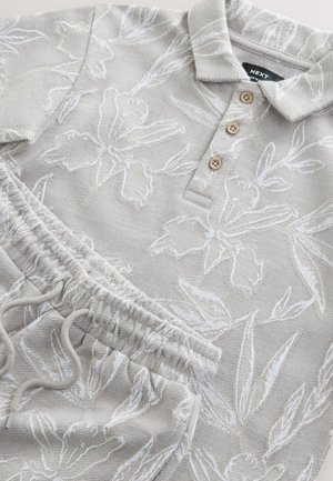 Jasnoszara bluza z białym kwiatowym wzorem i trójprzyciskowym dekoltem; dopasowane joggery z elastycznym pasem i regulowanym sznurkiem.