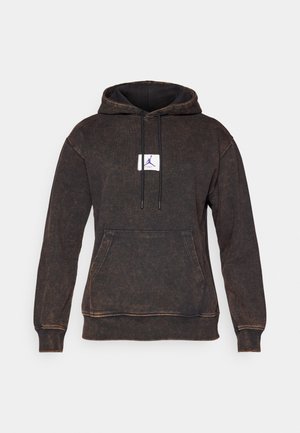 Sweatshirt à capuche en texture denim marron foncé. Comprend une poche avant, des cordons de tirage noirs et une étiquette blanche avec un logo violet.