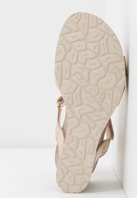Semelle de sandale avec motif de bande de roulement en caoutchouc beige, vue de face, brides latérales partiellement visibles sur fond blanc uni.