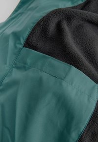 Nahaufnahme eines dunkelblauen Stoffpanels, das auf schwarzen Fleece-Stoff genäht ist, wobei Textur und Nahtdetails hervorgehoben werden.