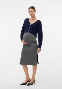 Cardigan tricoté marine avec trois boutons, associé à une jupe grise mi-longue avec des fentes sur les côtés, et des chaussures à talons noires.