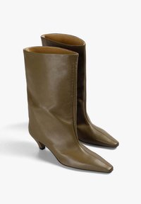 Par de botas de cuero marrón hasta la mitad de la pantorrilla con punta afilada y tacones bajos tipo kitten, exhibidas sobre un fondo blanco liso.