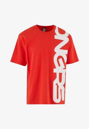 Piros pamut póló rövid ujjakkal, amelyen bal oldalon nagy fehér grafikai mintázat található. Kerek nyakú és laza fazonú.