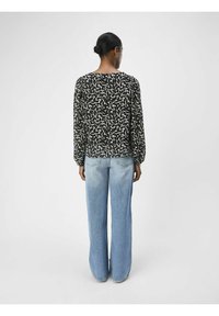 Blouse noire à manches longues avec un motif de feuilles blanches, associée à un jean taille haute bleu clair à jambe large, offrant une coupe décontractée et une texture douce.