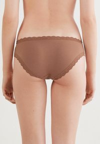 Bruine hipsteronderbroek met kantafwerking, gemaakt van een gladde stof en voorzien van een golvende rand, ontworpen voor comfort en een aansluitende pasvorm.