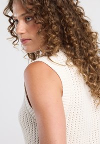 Cream-colored knit sleeveless top with a textured pattern, ribbed edges, and a fitted design. Smooth fabric and slight drape.