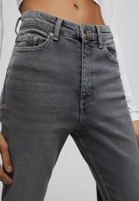 Jeans in denim grigio con vestibilità slim, vita media, cinque tasche e cuciture visibili, caratterizzati da una texture liscia e un leggero sbiadimento.