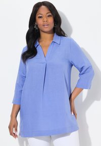 Top azzurro chiaro con colletto e scollatura a V, dotato di maniche tre quarti e un delicato dettaglio plissettato; texture liscia e leggero lucido.