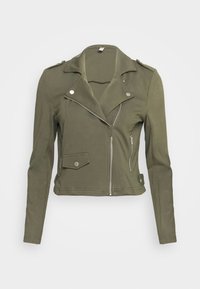 Giacca cropped verde oliva in un tessuto liscio, caratterizzata da un colletto a revers, una cerniera asimmetrica e una tasca a pattina con dettagli in metallo argentato.