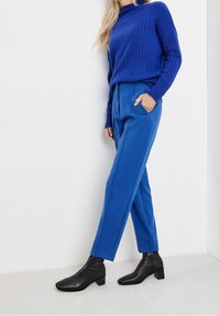 Blå ribbad tröja i kombination med klara blå byxor med sidofickor och svarta ankelskor med fyrkantig tå.